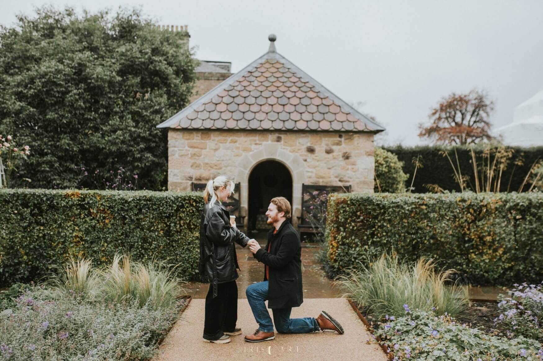 Man down on one knee proposing in Royal Botanic Gardens in Edinburgh surrounded by greenery