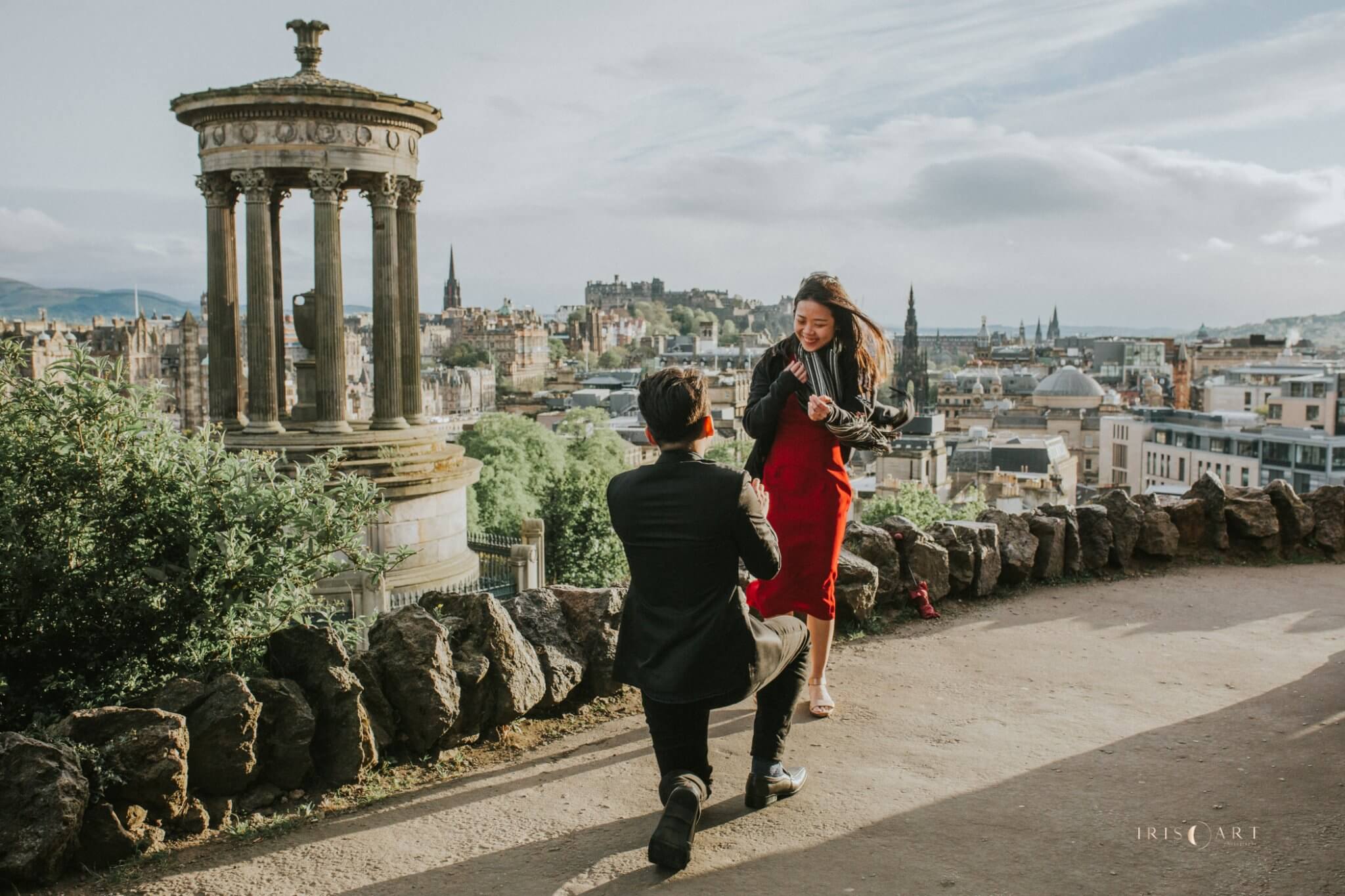 Man down on one knee proposing on top of Calton Hill in Edinburgh with amazing city view in the background