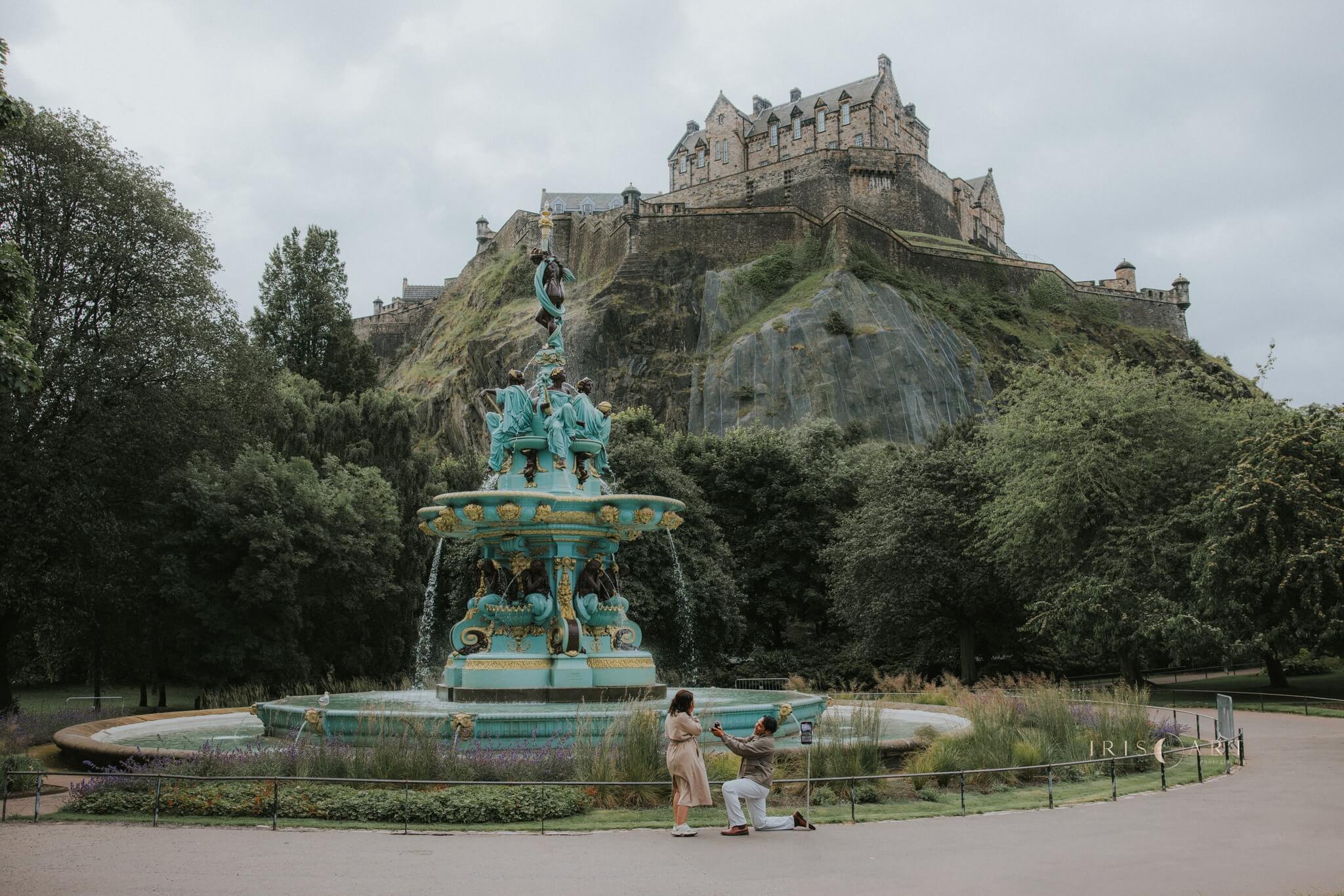 Man down on one knee proposing in front of Ross Fountain in Edinburgh with castle rock and Edinburgh Castle in the background