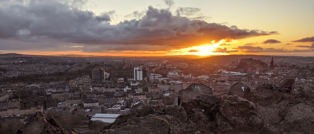 Sun setting over Edinburgh skyline with dramatic skies from Arthurs Seat