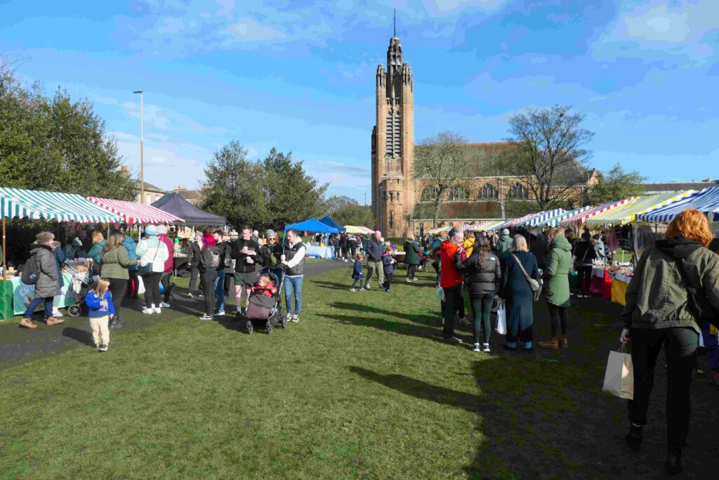 Busy stalls at Portobello Local Market, Edinburgh with St. John The Evangelist church in the background