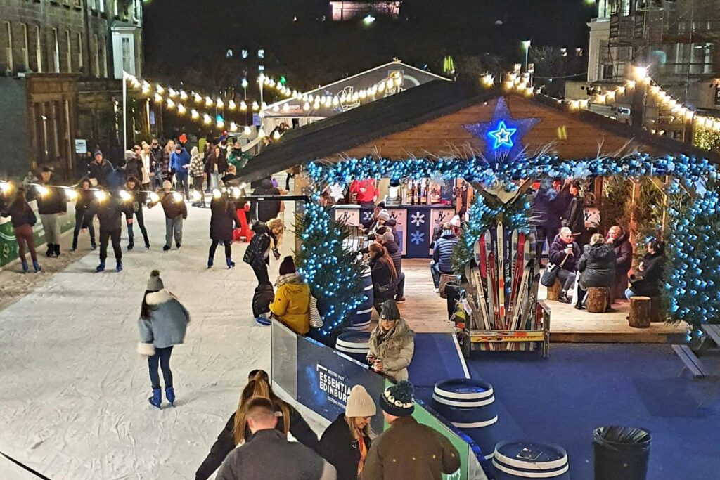people skating in front of an ice rink hut on edinburghs george street at christmas