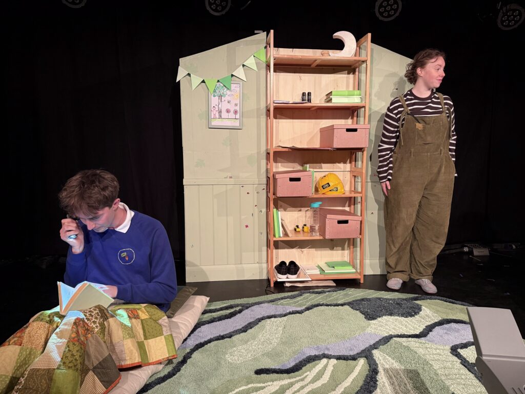 two actors on stage on opposite sides, looking away form one another with a wardrobe prop in the middle